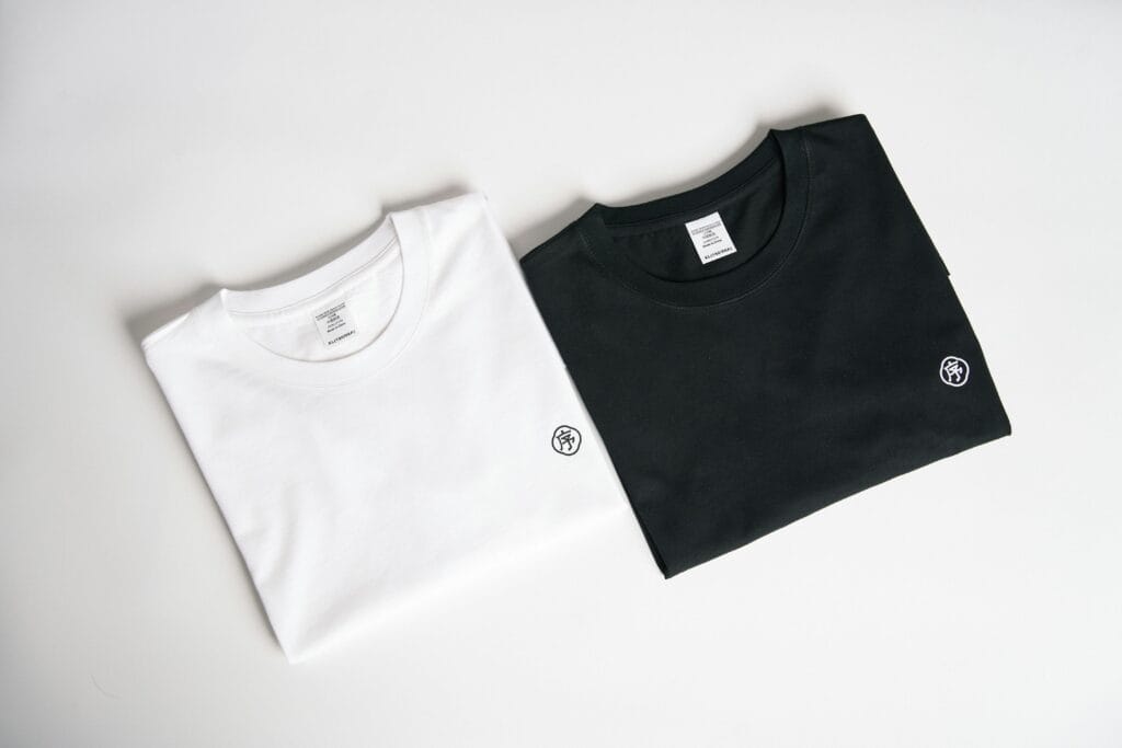 Textile Two folded t-shirts, one black and one white, on a plain background in a minimalist style.